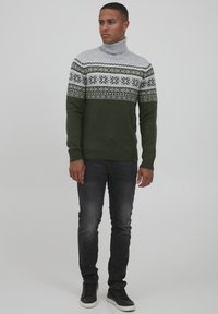 Pulover turtleneck verde închis, cu o yoke modelată gri care prezintă detalii cu fulgi de zăpadă. Manșete și tiv strâmte, asortat cu blugi negri și adidași negri.