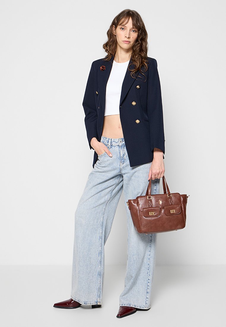 Blazer bleu marine à double boutonnage, top court blanc, jean large bleu clair, et sac à main en cuir marron avec des accents dorés. Chaussures pointues rouge foncé.