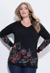 Czarna bluzka z długim rękawem i dekoltem w serek; posiada kwiatowe hafty w odcieniach czerwieni i niebieskiego na rękawach i u dołu. Miękki materiał, luźny krój.