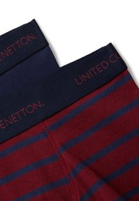 Dvě dvojice pruhovaných pánských boxerů v burgundské a námořnické barvě s tmavě modrými elastickými pásky, na kterých je text "United Colors of Benetton".