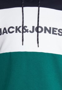 Sudadera con capucha que presenta un diseño de bloques de color en azul marino, blanco y verde, con un destacado logo negro de "JACK&JONES" y cordones de contraste.