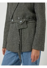 Getailleerd grijs-zwart gestreept jasje met een double-breasted ontwerp, knoopdetails en een ceintuurdetail in de taille.