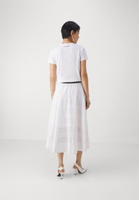 Tricou alb cu mânecă scurtă și un design cropped, purtat cu o fustă lungă albă, cu modele brodate și decupaje.