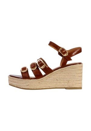 Sandale compensée en cuir brun avec trois sangles ajustables, boucles en or et plateforme en jute tressé. Fini lisse et design à bout rond.