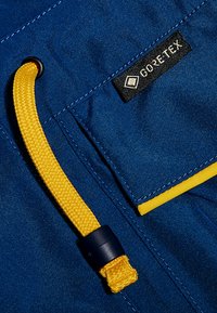 GORE-TEX-Gewebe in tiefblau mit gelben Kordeldetails. Verfügt über eine strukturierte Oberfläche und kontrastierende gelbe Akzente an den Kanten.