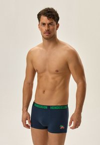 Granatowe bawełniane majtki typu trunk z zielonym elastycznym pasem w talii, na którym znajduje się napis "Henderson" oraz mała grafika czerwonego samochodu z motywem drzewa.