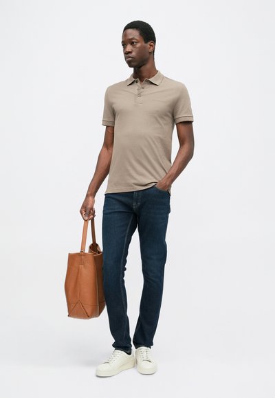 Barna pólóing, sötét farmernadrág, fehér sportcipő, barna bőr válltáska a kezében. Egyenes szabású, rövid ujjú, klasszikus gallérral.