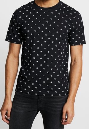 Zwart katoenen T-shirt met een herhaald wit logopatroon. Korte mouwen, ronde hals en een aansluitend ontwerp. Gecombineerd met een donkere spijkerbroek.