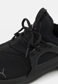 Scarpa sportiva nera con tomaia in rete, pannelli testurizzati, collare imbottito e lacci piatti, con un logo del marchio ben visibile sul lato.