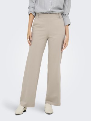 Pantalons beige à jambes larges avec une texture lisse, taille haute et poches latérales. Associés à une chemise à rayures légères et des chaussures blanches.
