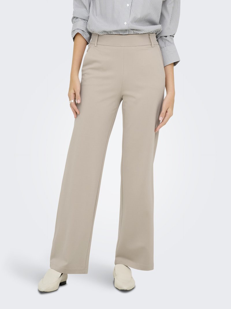 Pantalons beige à jambes larges avec une texture lisse, taille haute et poches latérales. Associés à une chemise à rayures légères et des chaussures blanches.
