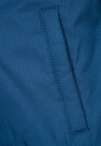 Mörkblått tyg med ett hexagonmönster, med platta sömmar och en sidoficka. Texturen verkar slät och lättviktig.