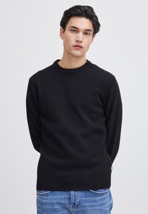 Pull noir à col rond fabriqué en matériau doux, présenté avec des manches longues et un ourlet côtelé. Assorti à un jean bleu clair.