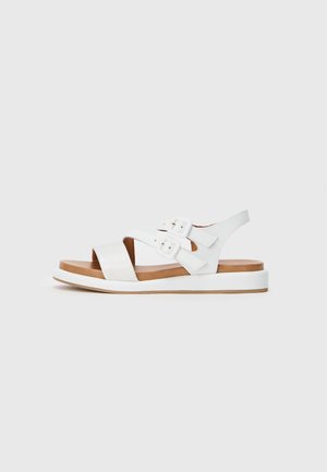 White sandal with two adjustable buckle straps, a crossover front design, and a flat, textured sole. Accented with a light brown footbed.