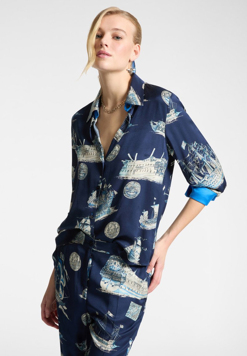 Camicia di seta blu navy con stampe nautiche di navi e luoghi storici, con polsini azzurri a contrasto e un design dalla vestibilità rilassata.