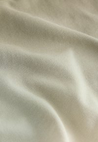 Béžová mäkká látka s jemnou pletenou textúrou a jemnými záhybmi vytvárajúce jemné tiene a svetelné odlesky.