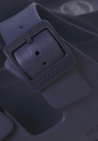Bracelet en caoutchouc bleu marine avec une boucle carrée, présentant un logo embossé sur le bracelet et deux trous d'ajustement pour un meilleur ajustement.