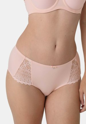 Frau trägt hellrosa Hipster-Panties mit Spitzenbesatz und passenden BH, gezeigt vom Bauch bis zu den oberen Oberschenkeln vor weißem Hintergrund.
