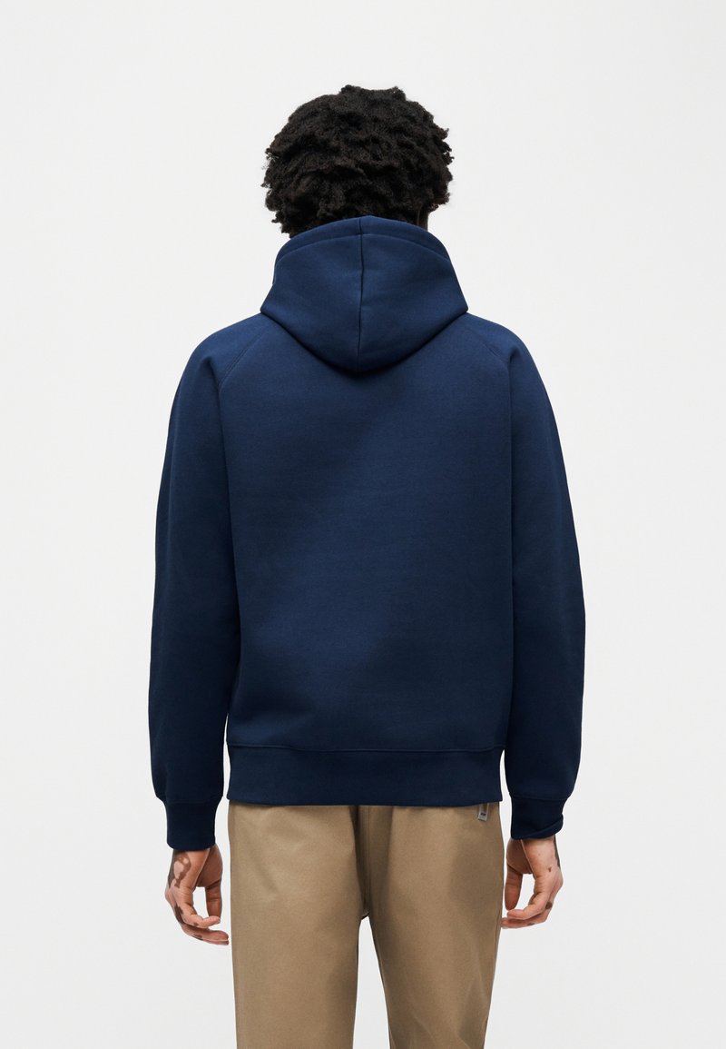 Sweat à capuche bleu marine avec une coupe décontractée, des poignets et un ourlet côtelés, une poche kangourou et une capuche à cordon. Texture unie sans logos visibles.