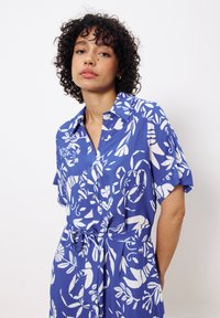 Blaues kurzärmliges Kleid mit weißem Blumenmuster, Hemdkragen, gebundenem Taillenband und leichtem Stoff, der einen lässigen Sitz bietet.