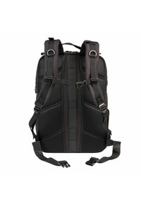 Mochila negra con respaldo de malla acolchada, correas ajustables y múltiples broches; forma rectangular con paneles texturizados y detalle de cintas en el centro.
