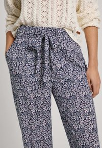 La partea de jos, pantaloni florali bleumarin cu talie cu șiret, având un model repetat de flori roz și albe și buzunare laterale. Fabricat dintr-un material ușor.