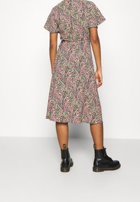 Blumiges Midikleid mit pinkem, grünem und lila Muster, kurzen Rüschärmeln und taillierter Passform, kombiniert mit schwarzen Knöchelstiefeletten.