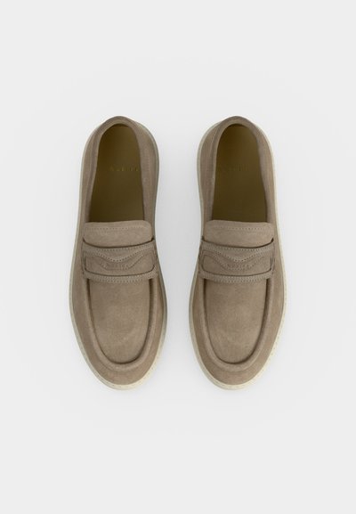 Paire de mocassins beige en daim à enfiler, avec des bouts arrondis et semelles en caoutchouc blanches, vus de dessus sur fond blanc.