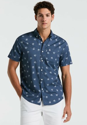 Chemise à manches courtes avec des boutons, de couleur marine, ornée d'un motif de feuilles de palmier blanches, avec une poche poitrine et un ourlet arrondi. Tissu en coton lisse.