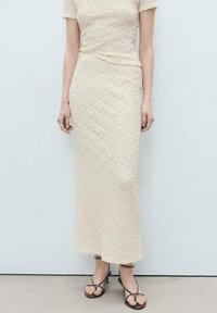 Robe créme à manches courtes, en tissu texturé, forme ajustée, jupe au genou et détails minimalistes. Portée avec des sandales à lanières.