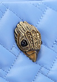 Pelle trapuntata blu chiaro con una chiusura a forma di uccello in metallo dorato, decorata con strass e un occhio di gemma scura.