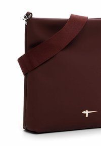 Pruun silikoonist rinna- või õlakott, millel on läikiv kuldne detail ja lai kangast rihm. Omaduseks on stiilne ristkülikukujuline kuju ja sile pind.