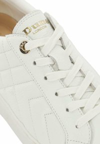 White leather sneaker with textured surface, featuring a quilted pattern, white laces, and gold branding detail on the tongue.