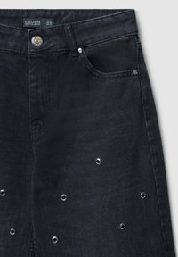 Jeans en denim noir avec des détails en œillets argentés et une fermeture à bouton. Comprend des poches avant standard et une étiquette à la taille.