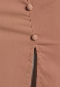 Persikofärgad tyg med en slät yta, utrustad med två tygklädda knappar och en sidoflik. Fin sömnad längs kanterna.