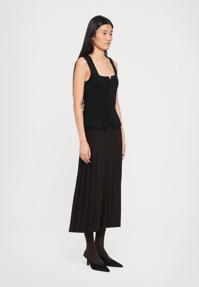 Black sleeveless vest with square neckline and five-button closure, paired with a long pleated black skirt. Model wears black heels and tights.
