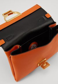 Borsa strutturata in pelle arancione con texture, dotata di una parte superiore nera, chiusura in hardware dorato e un accento circolare.