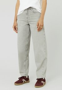 Jean taille haute gris clair, avec une coupe ample, comportant des poches latérales et une ceinture standard. Associé à des baskets bordeaux.