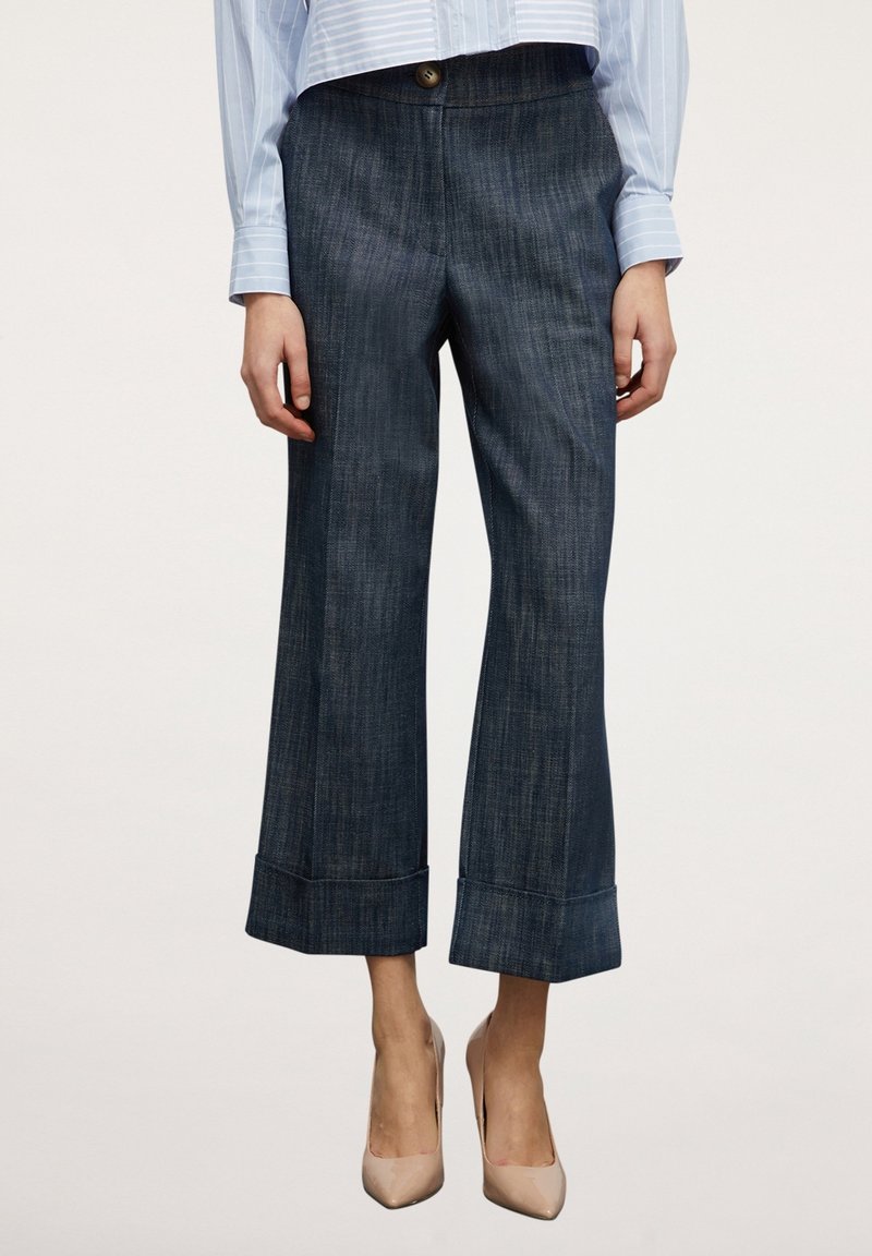 Pantalon court en denim bleu marine avec une coupe droite, revers pliables, fermeture à boutons sur le devant, et une texture verticale subtile.