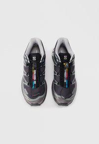 Schwarze Sportschuhe mit grauen Akzenten, Obermaterial aus Mesh und schnellschnürendem System. Verfügt über ein gepolstertes Innenleben und eine strukturierte Gummisohle. Markenlogo sichtbar.