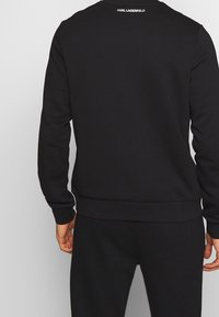 Czarna bluza wykonana z miękkiego materiału, z okrągłym dekoltem, ściągaczami na mankietach i dole. Logo na plecach przy linii szyi.