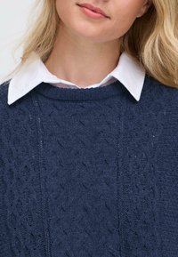 Marineblaue Kabelstrickpullover mit strukturiertem Muster, Rundhalsausschnitt und einem schichtweisen weißen Kragen. Weiches Strickmaterial, lässiges Design.