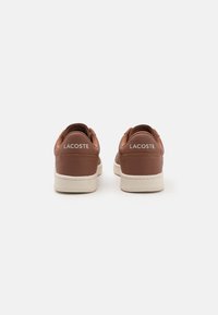 Smeđe kožne tenisice s bijelom potplatom, s glatkom teksturom i Lacoste logotipom na peti.
