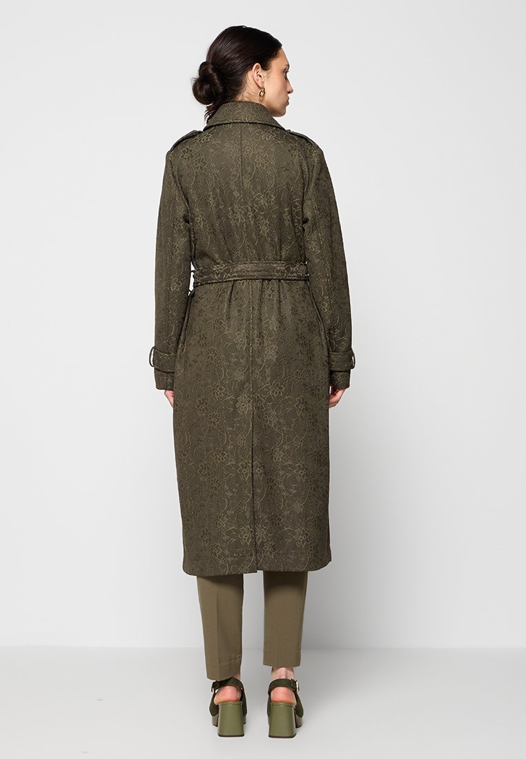 Trench coat verde oliva con texture a motivo floreale, vita cinturata e maniche lunghe. Progettato con colletto classico e spacco posteriore.