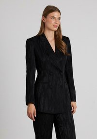 Blazer negro de doble botonadura con un patrón texturizado, ajuste entallado, solapas de muesca y dos botones, combinado con pantalones a juego.