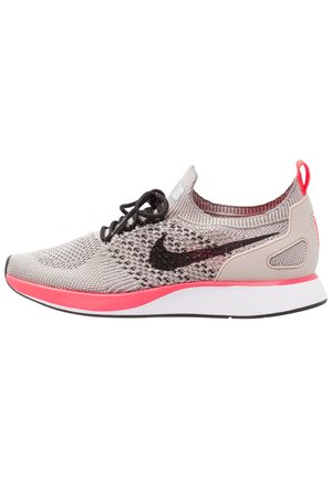 Lysegrå strikket løbesko med sorte snørebånd, sort Nike-swoosh, koralfarvede accenter på sålen og hæl-løftetab samt hvid mellemsål.