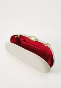 Beige clutch taske med rund form og gyldent hardware. Indvendigt er den foret med rød satin og har en lille lomme.