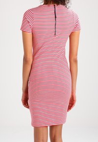 Randig klänning med korta ärmar, röda och vita horisontella ränder, en figurnära silhuett och en svart dragkedjedetalj på baksidan.