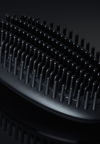 Zwarte plastic haarborstel met rijen flexibele borstelharen, afgeronde punten en een afgeronde ovale basis voor ergonomische grip. Glad oppervlak.