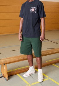 Czarny t-shirt z grafiką "Nike Hoops", zielone szorty oraz białe wysokie trampki. Gładka tkanina; swobodny, sportowy styl; prosty wzór.